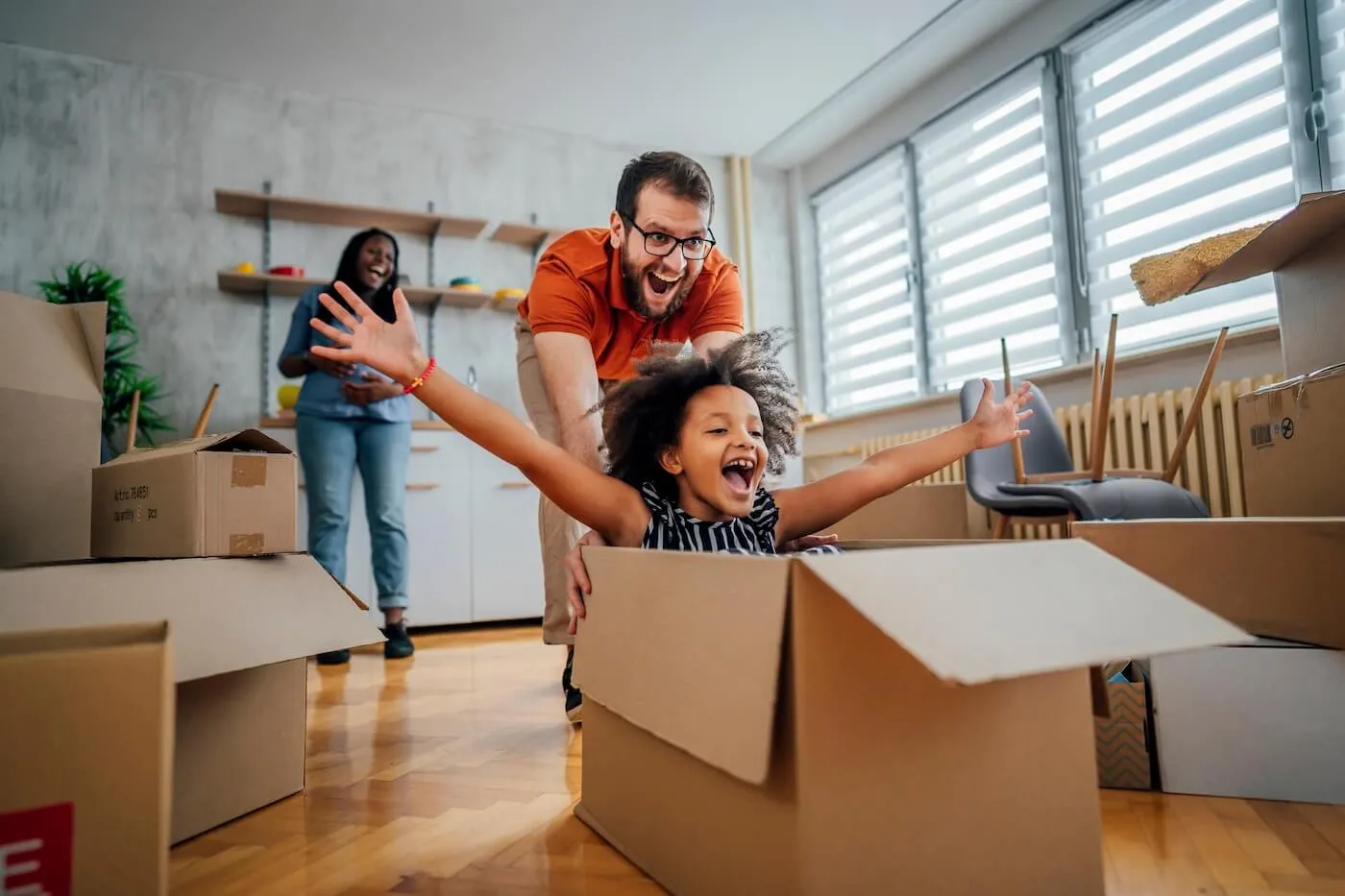 A young family of three playing with the moving boxes in their new living room