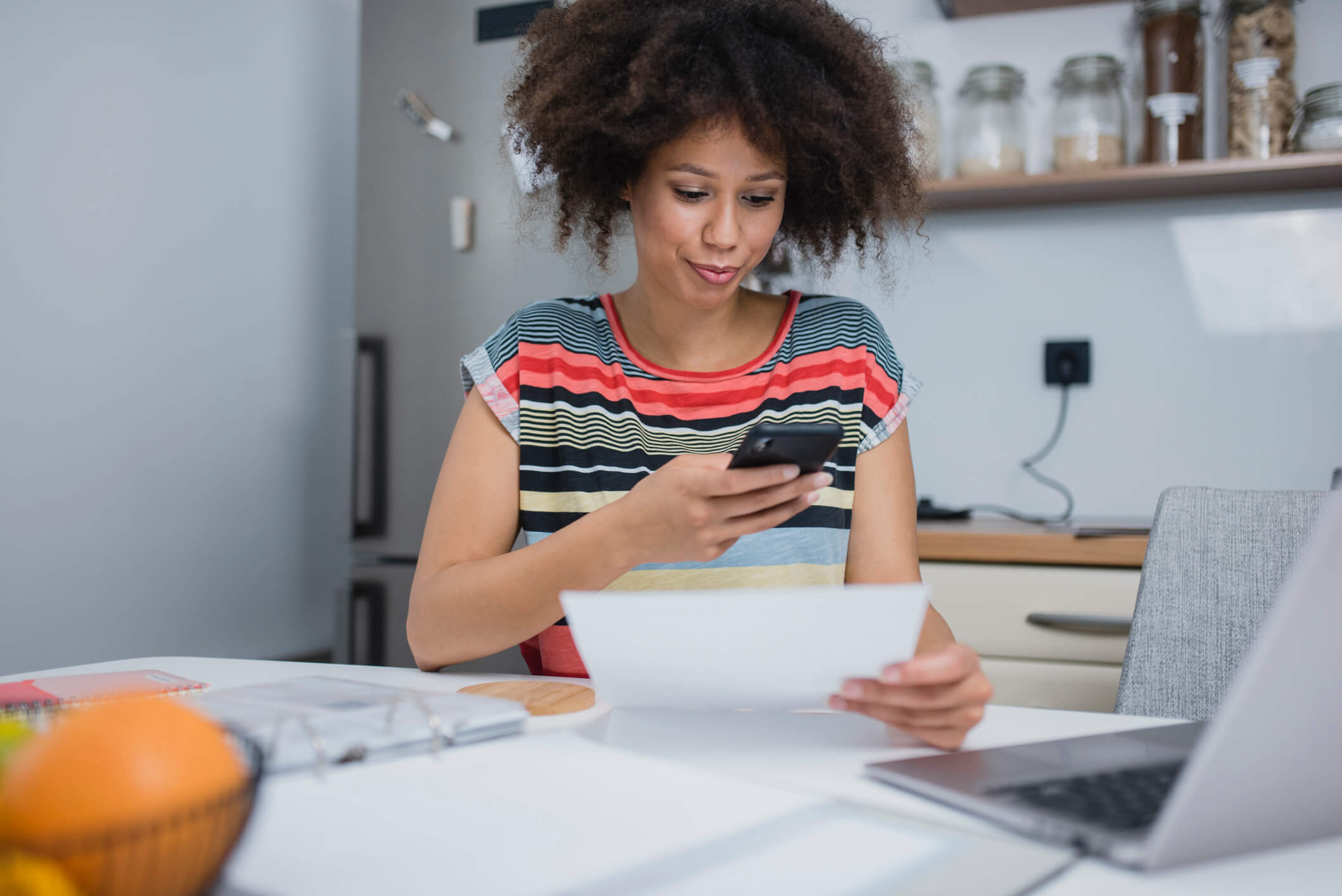 Woman checking her phone at her desk while holding printed documents