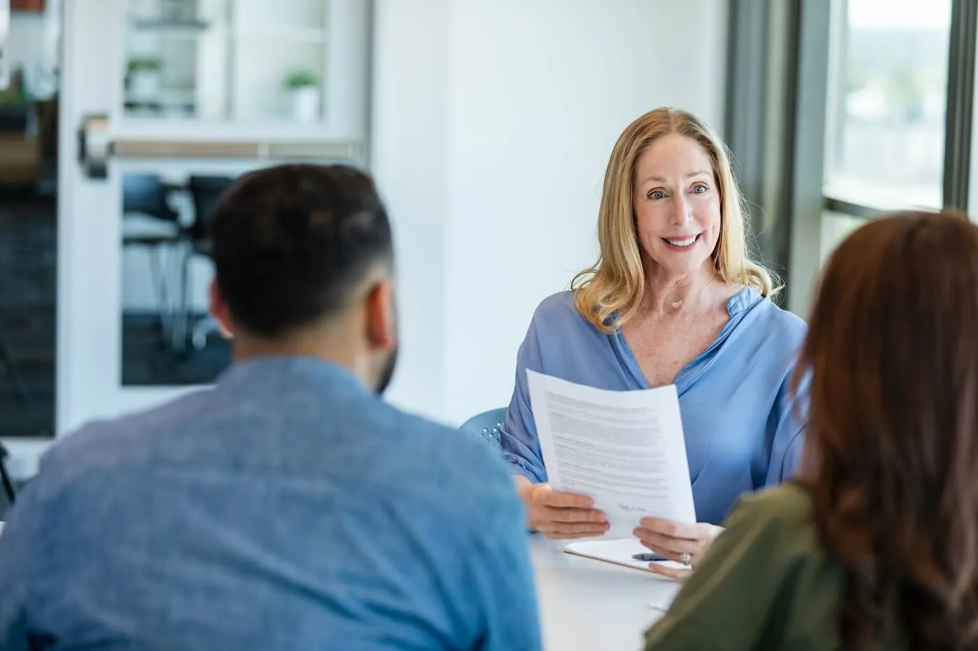 Smiling female bank employee explaining loan terms to a couple seated across from her at a desk
