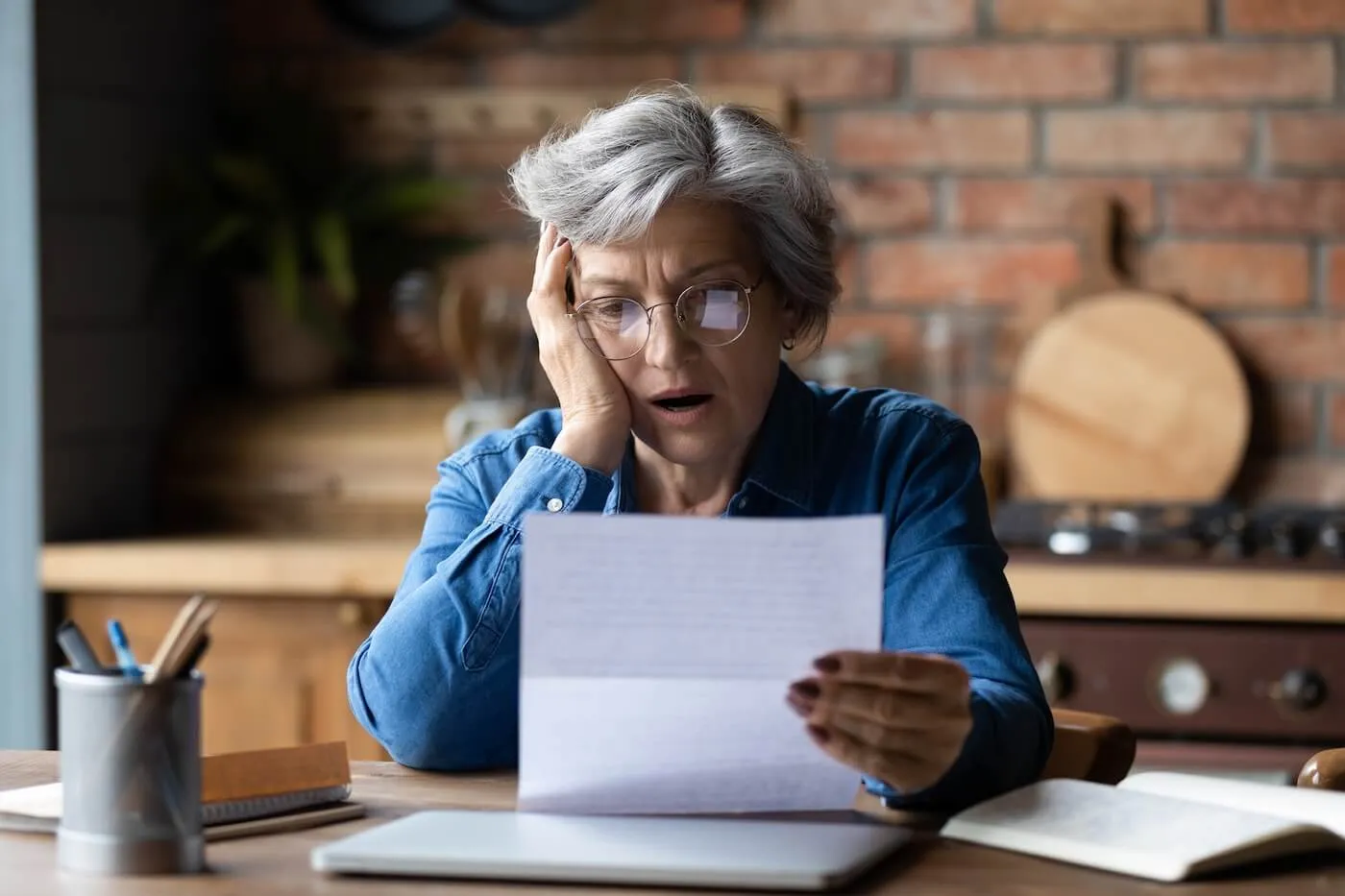 Shocked senior woman looking at her bills at home