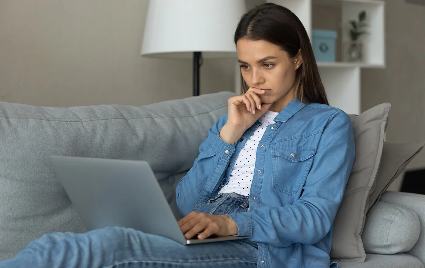 Concerned young woman sitting on a sofa with a laptop
