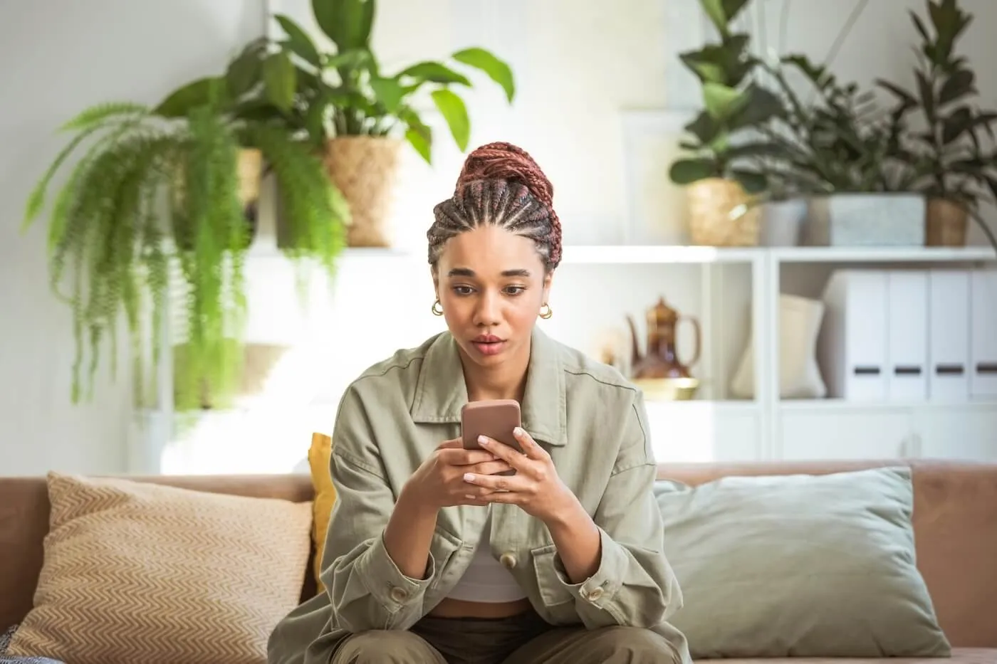 Concerned young woman sitting on a sofa in the living room, checking her emails on a smartphone