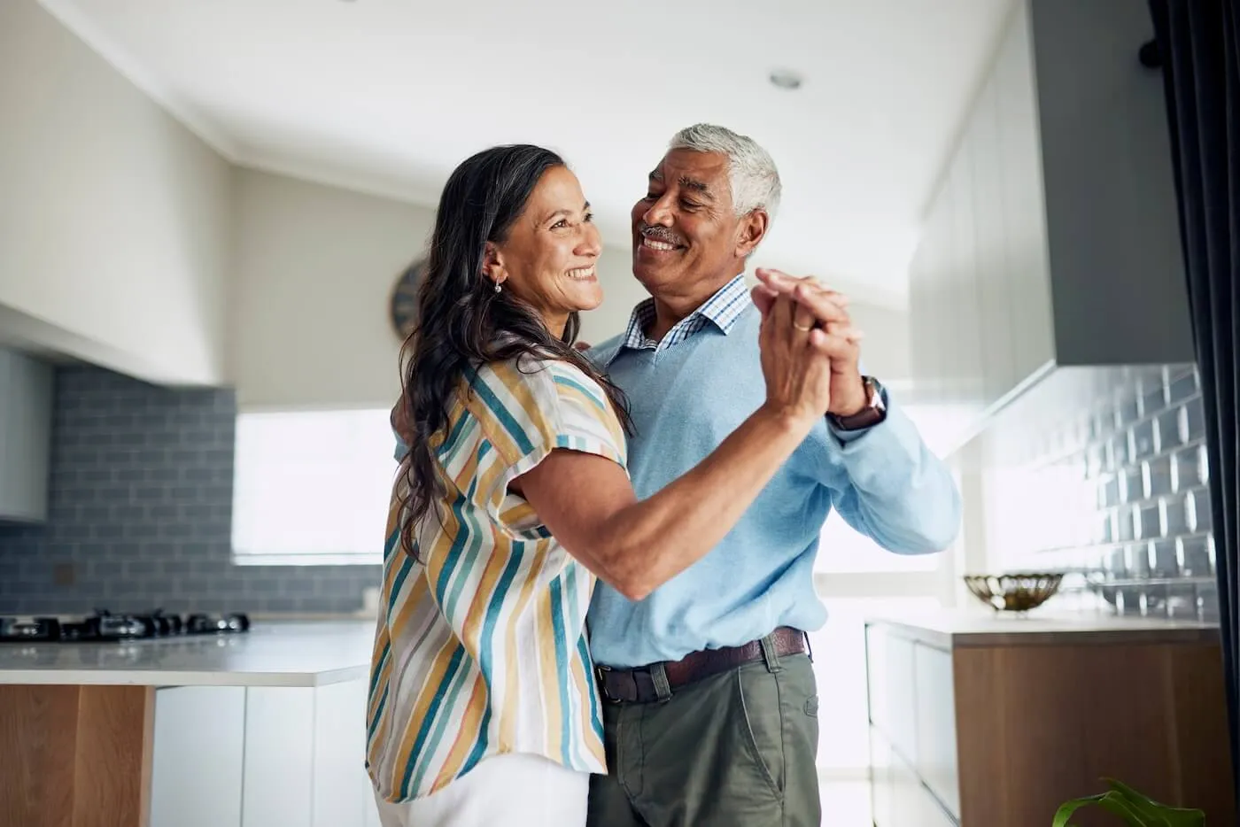 A happy elderly couple is dancing in the kitchen.