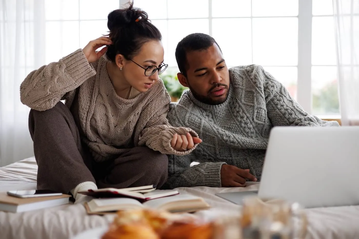 Focused couple in cozy outfits sitting on the bed with an open laptop, discussing mortgage rates