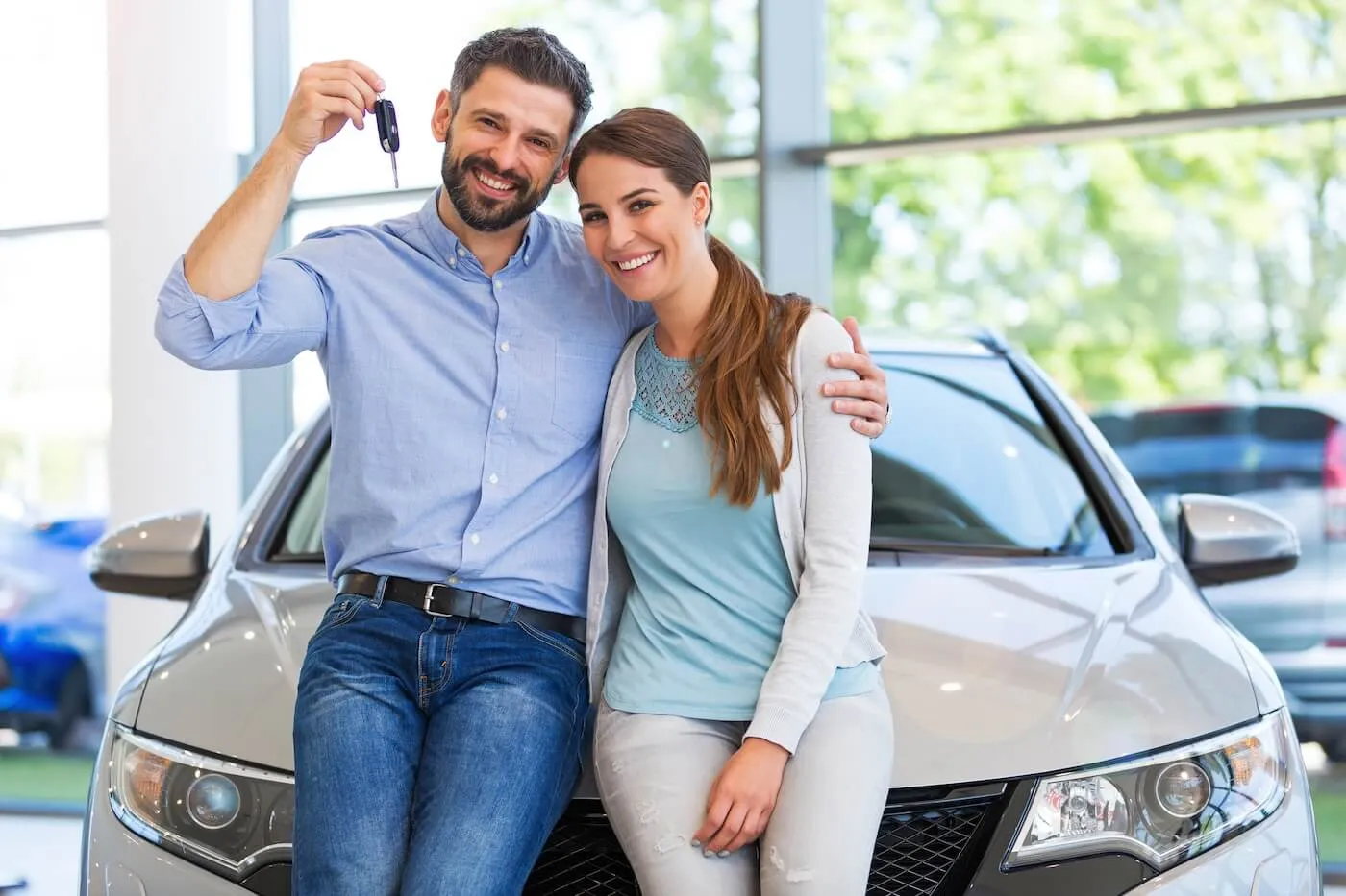 Photo of a happy couple sitting on the hood of their new car and holding the car keys