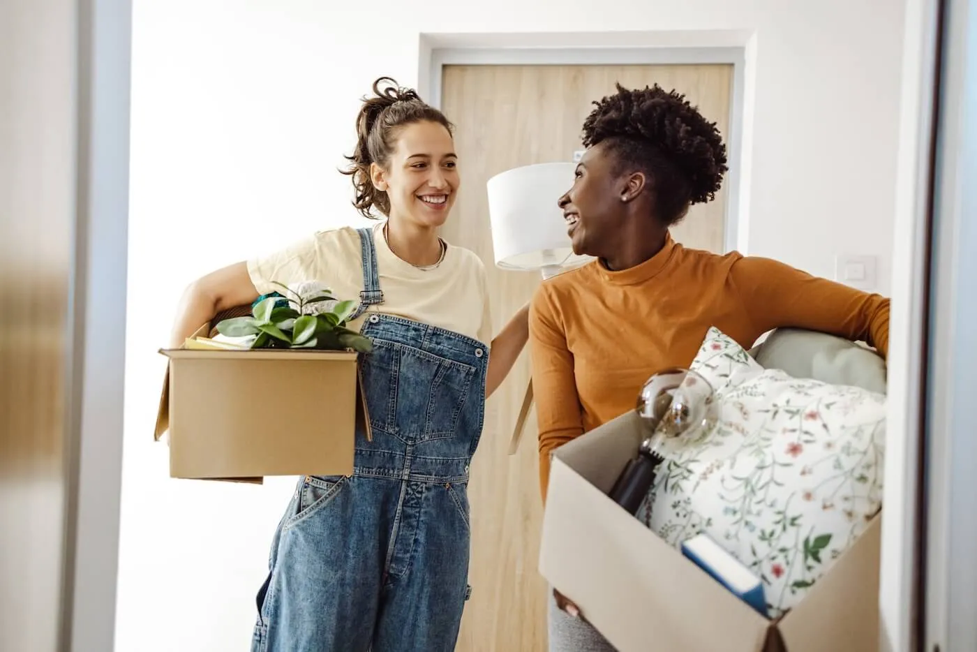 Two smiling female flatmates entering their new home with the moving boxes