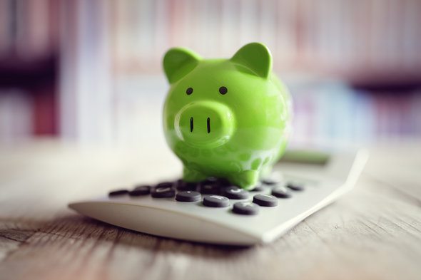 A small green piggy bank sitting on top of a calculator.