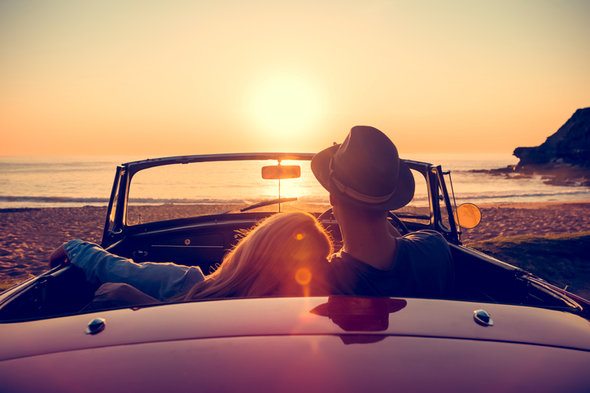 A couple watch a sunset from their car.
