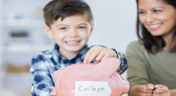 A mother watches her son put money in a piggy bank labeled "college."