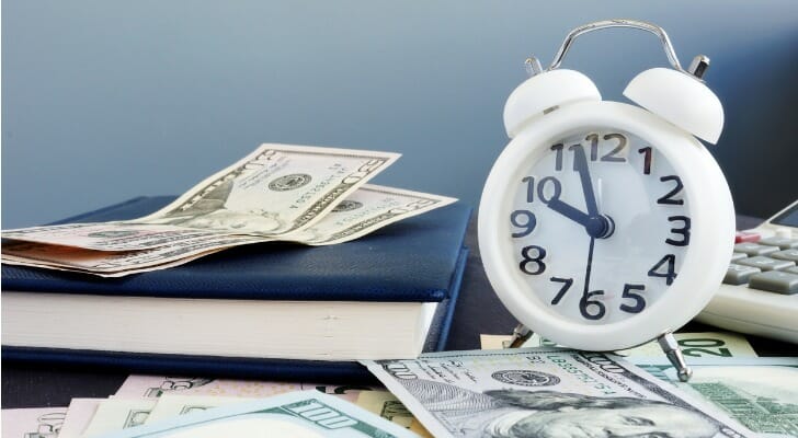 A clock, calculator, and money sitting on a desk.