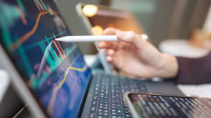 A person holds a pen to the screen of their laptop and reviews a graph.